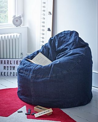 A blue denim bean bag in a room with white walls and white wooden floors.