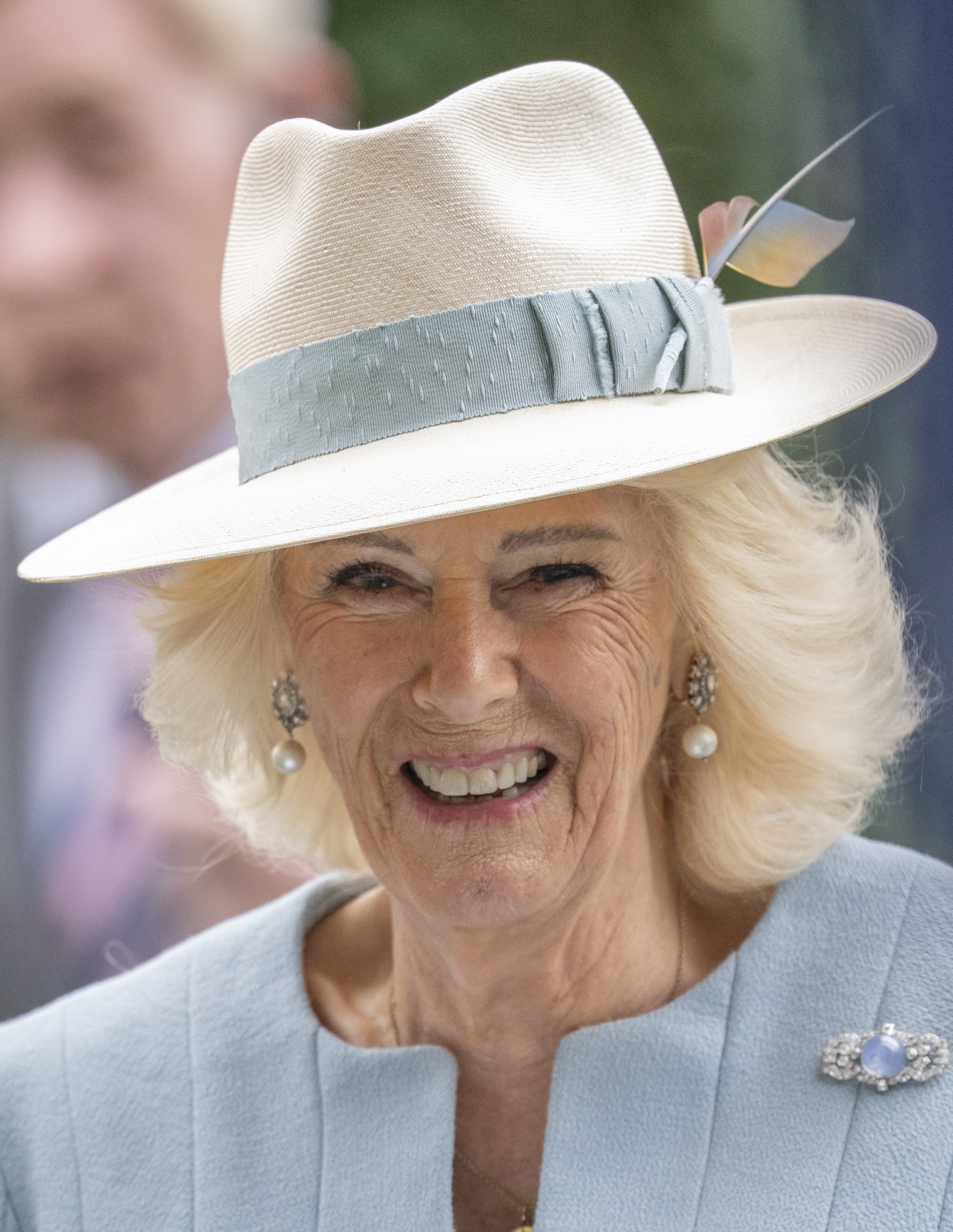 Queen Camilla wearing a fedora with a blue band and pale blue coat