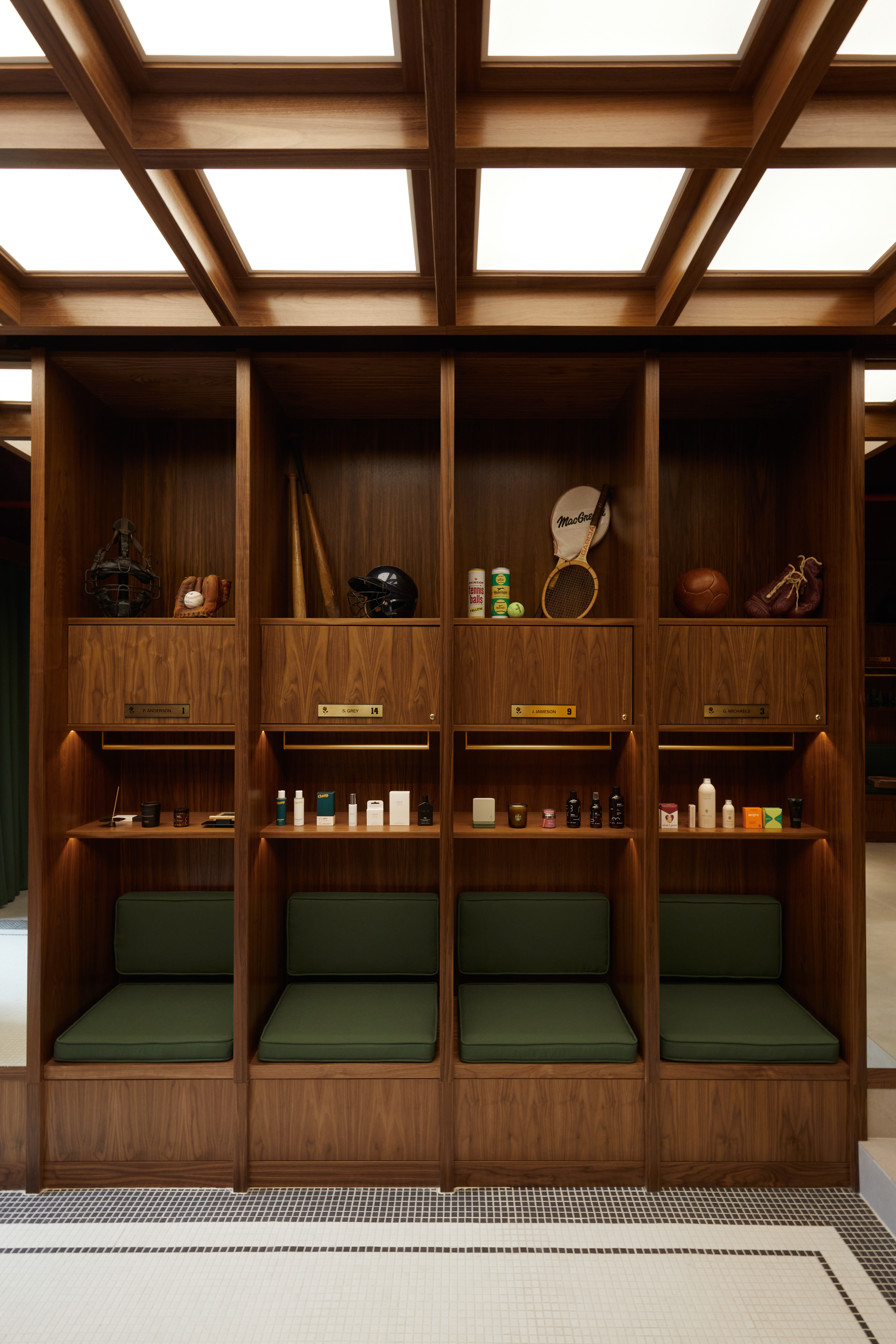 A locker room-looking, retro-inspired shop features a wood and emerald green 1970s-style palette, paneled walls with built-in shelves stacked with sports heirlooms, and chairs.