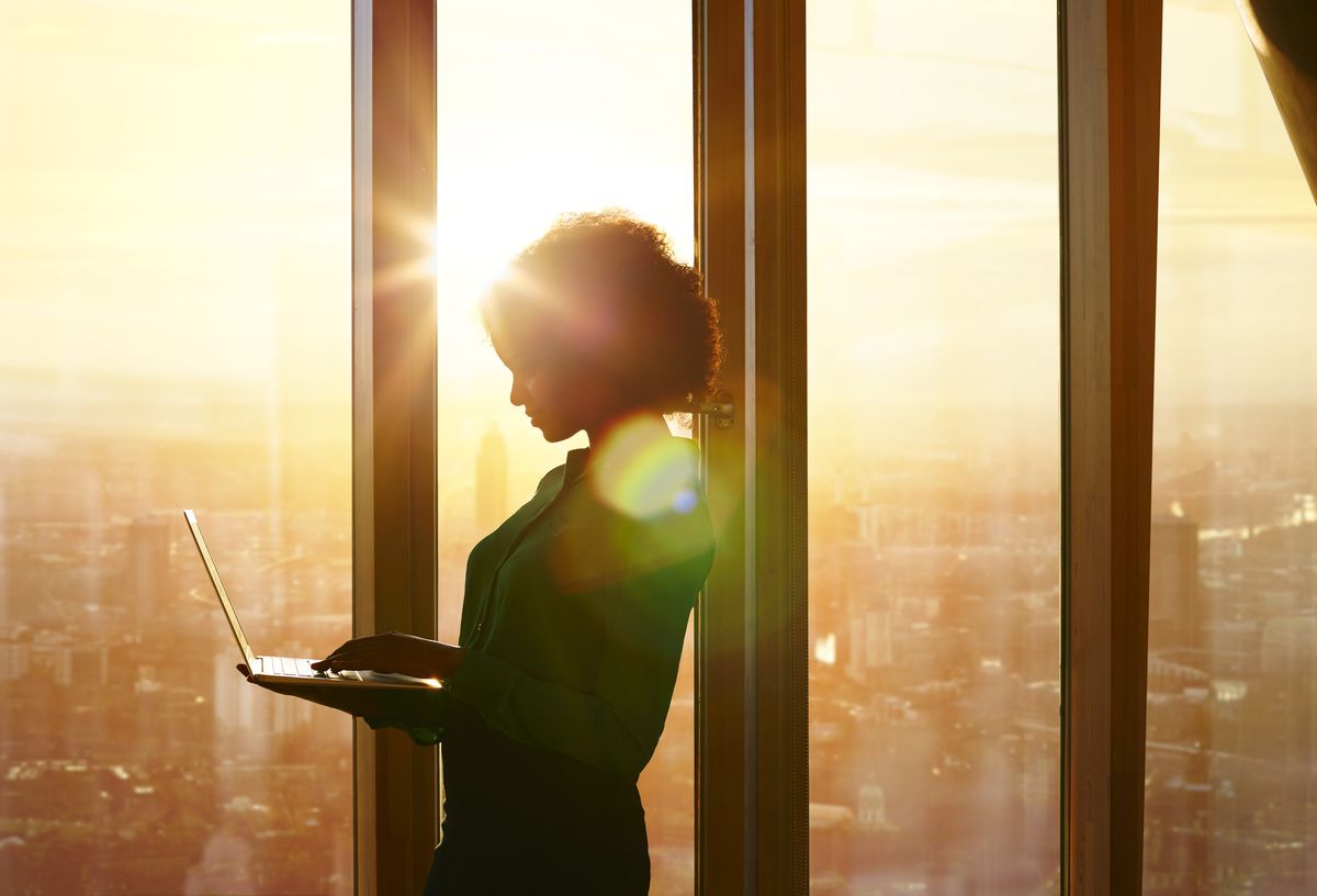 A woman staring at her laptop with the sunrise in the background