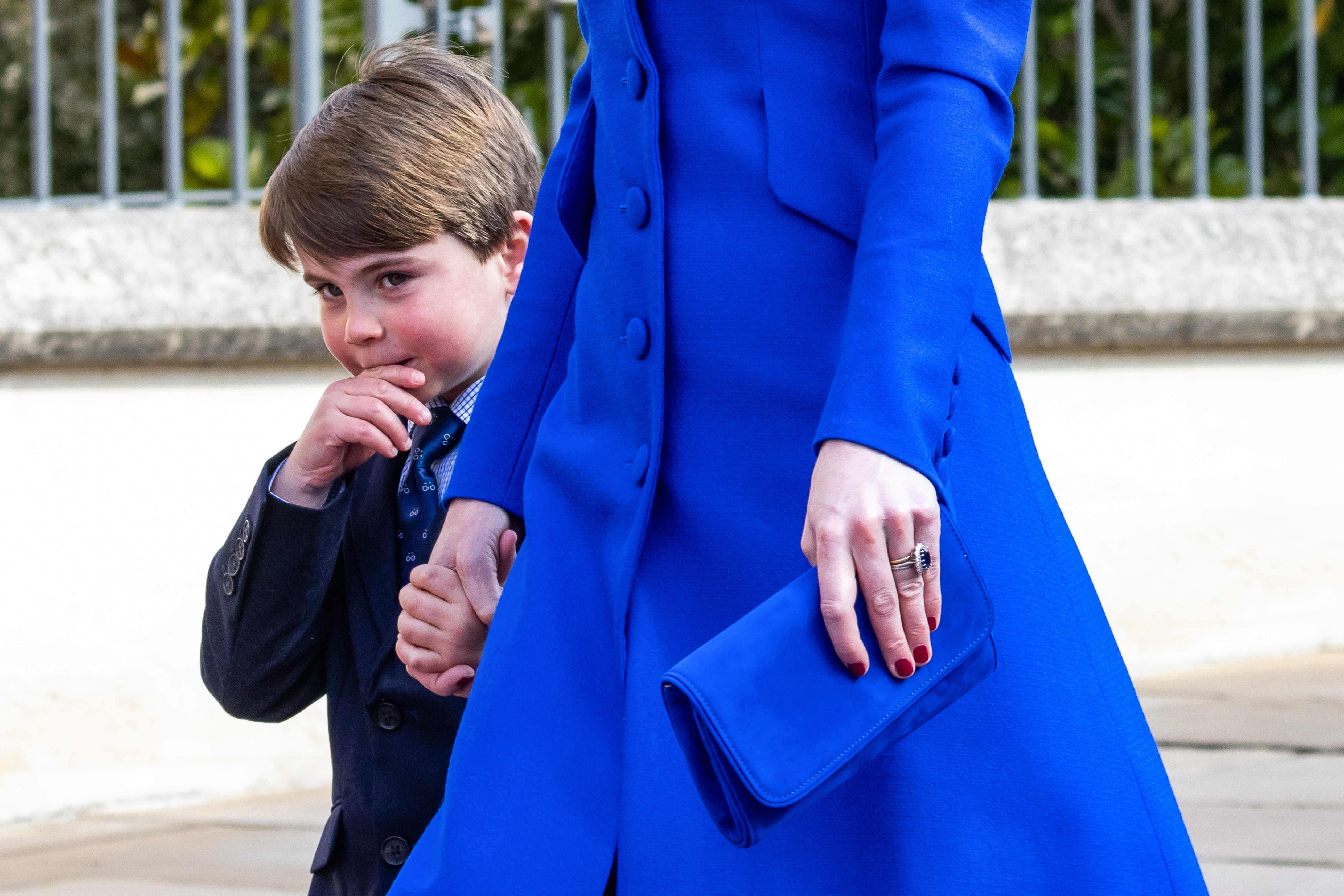 Closeup of Kate Middleton&#039;s blue coat and red nails holding a clutch and Prince Louis&#039;s hand