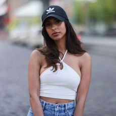 Dionne Roeder is seen wearing a white top, a blue denim jeans, a black Chanel leather clutch, and black sunglasses and a summer hat and colorful sneakers on May 06, 2022 in Berlin, Germany.