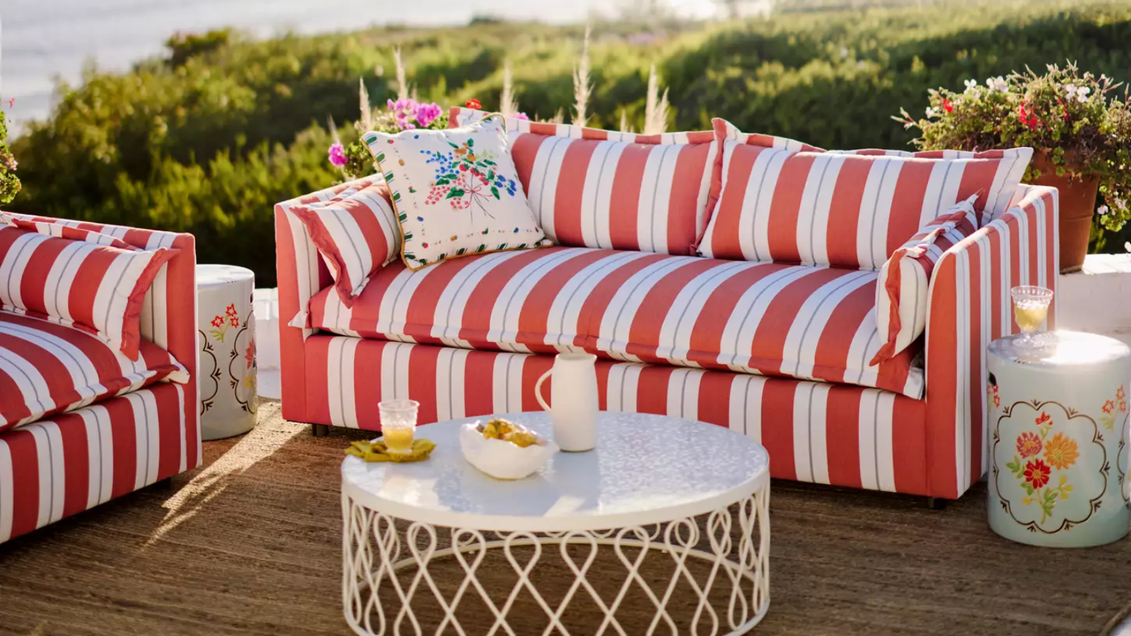 a red and white striped outdoor couch with a pillow on it, a white outdoor coffee table with decorative detailing around the sides, a jute rug, and a small accent table to the right of the couch