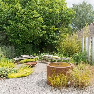 outdoor seating area with a corten steel round water feature, bench seating, wild grasses and a firepit