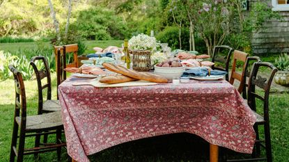 Outdoor dining table with mis-matched antique chairs, patterned tablecloth and plates of food