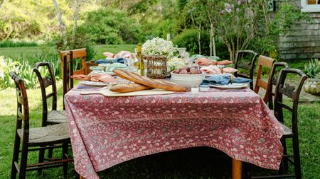 Outdoor dining table with mis-matched antique chairs, patterned tablecloth and plates of food