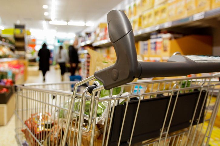 A shopping trolley with food inside of it in a supermarket aisle.