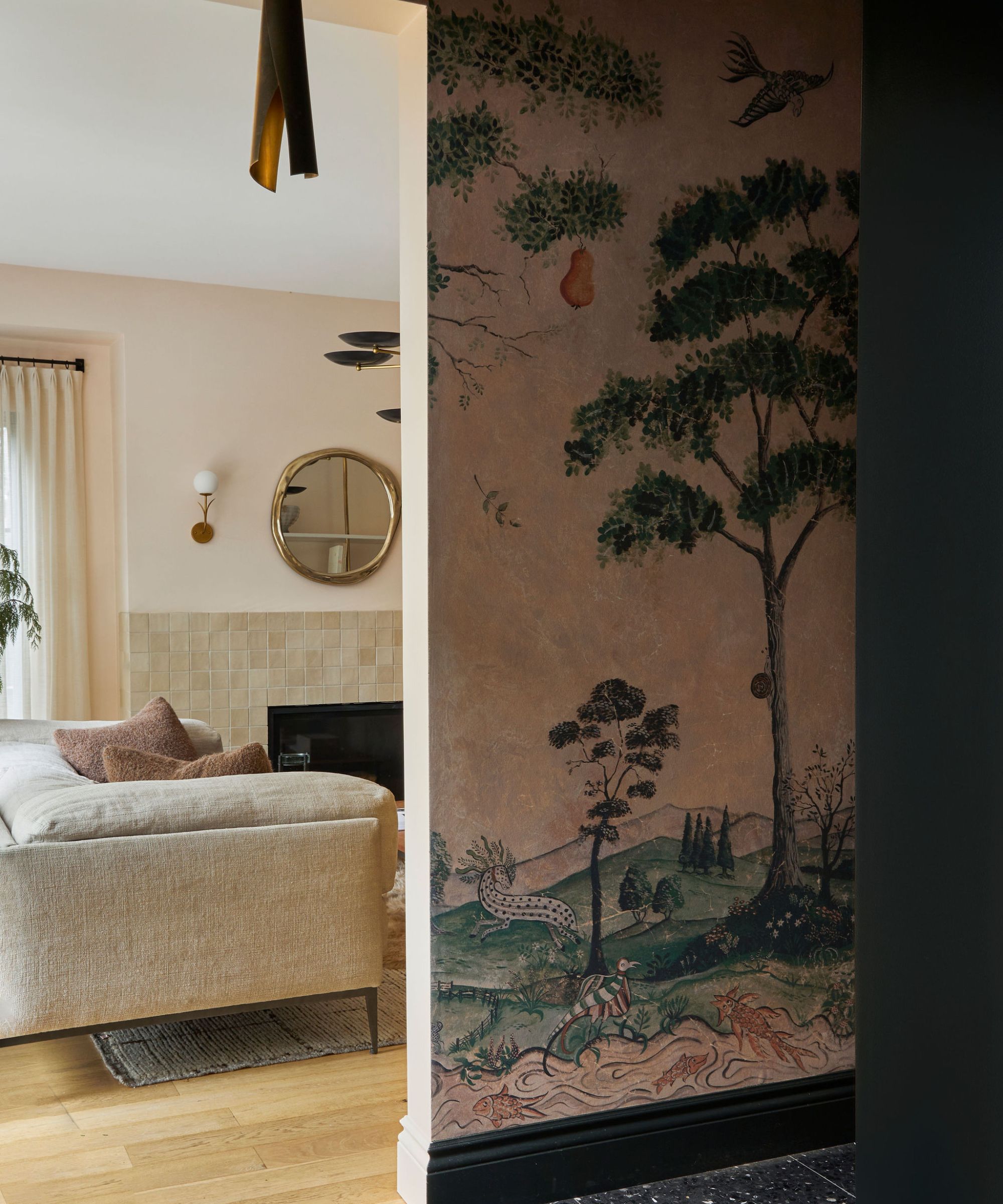 A neutral living room with large black metal windows taking up one wall. There is a large beige sofa with a dog sitting on it and a tree to the left hand side. In front is a large wooden coffee table