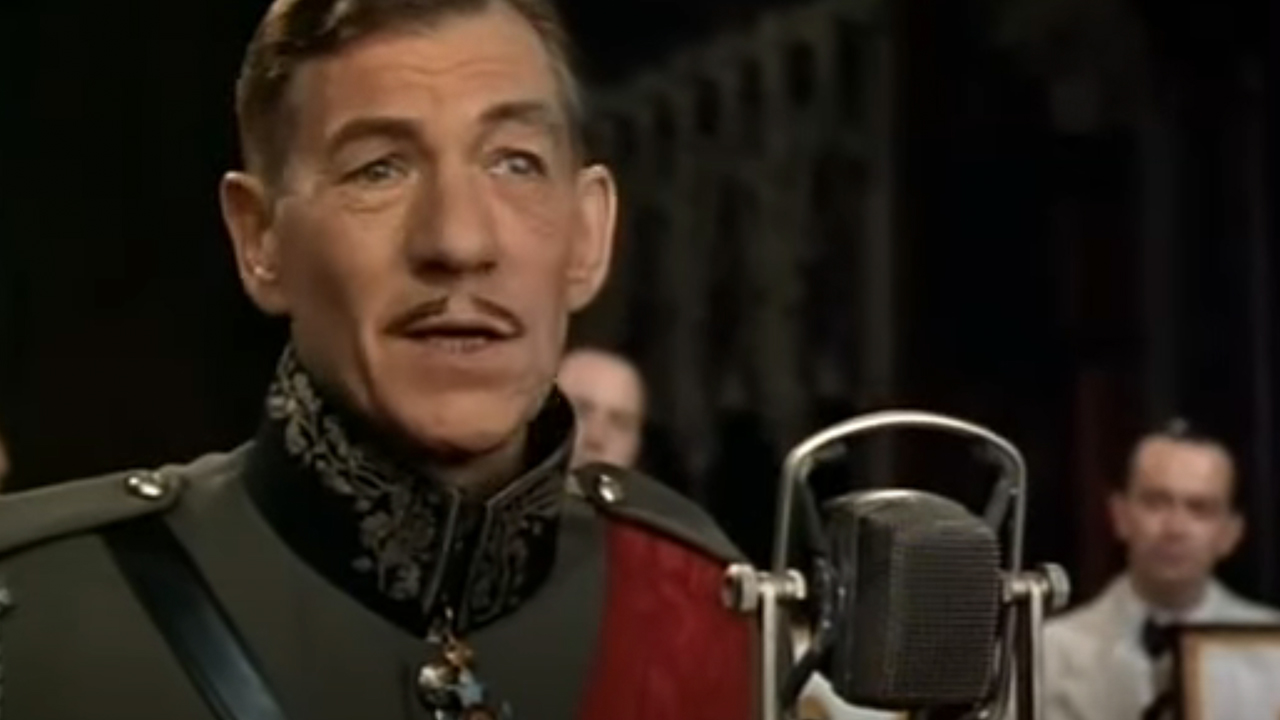 Ian McKellen in a 1930s military uniform speaking into an old-timey microphone.