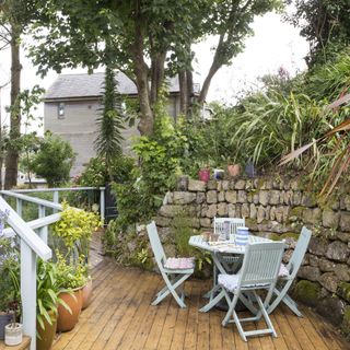 Garden patio with decking and curved stone wall, pale blue wooden folding chairs and table