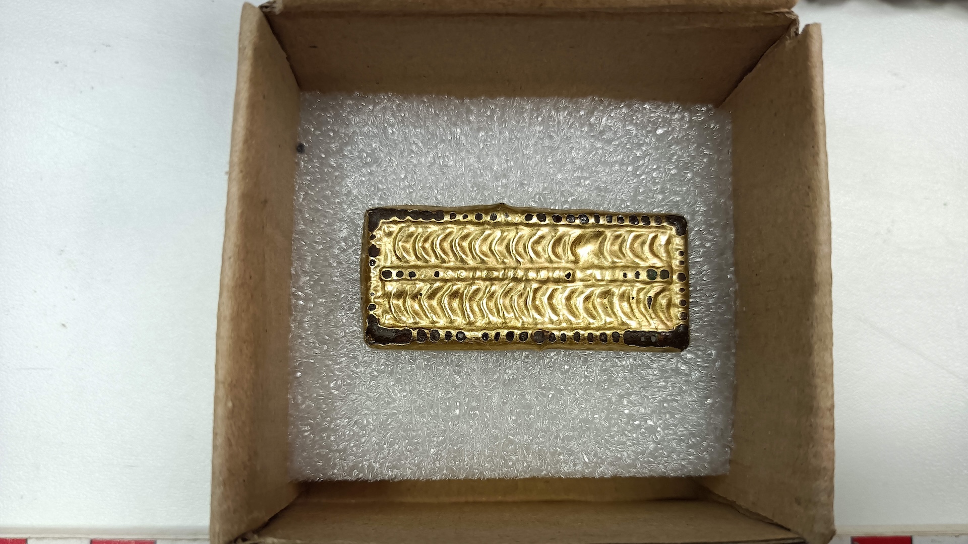 a gilded piece of decorated metal in a box