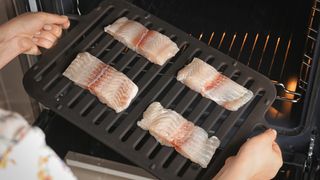 Woman putting broiler pan with fish fillet slices into oven