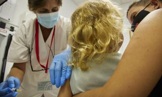 A young girl receives a vaccine from a doctor while being held by her mom in a clinic