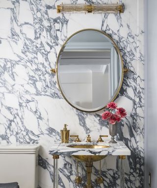 Detail of a powder room with marble clad walls and brass faucets