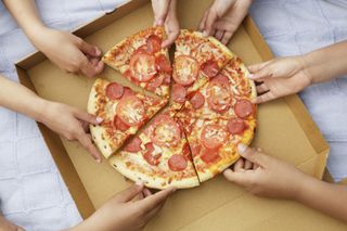 Children's hands each taking a slice of pizza from a cardboard pizza box.
