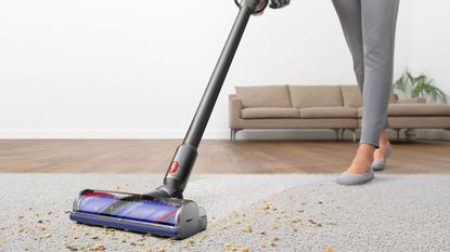 Dyson V8 vs Dyson V10: a Dyson V10 vacuuming cereal and debris off a gray carpet