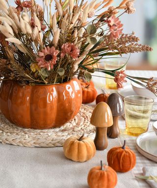 A table with a pumpkin vase with dried flowers, ceramic mushrooms and three small pumpkins on it