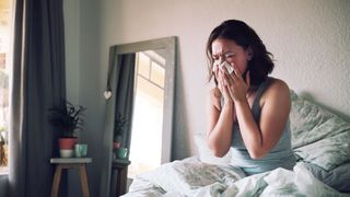 Woman blowing her nose in bed because of allergies
