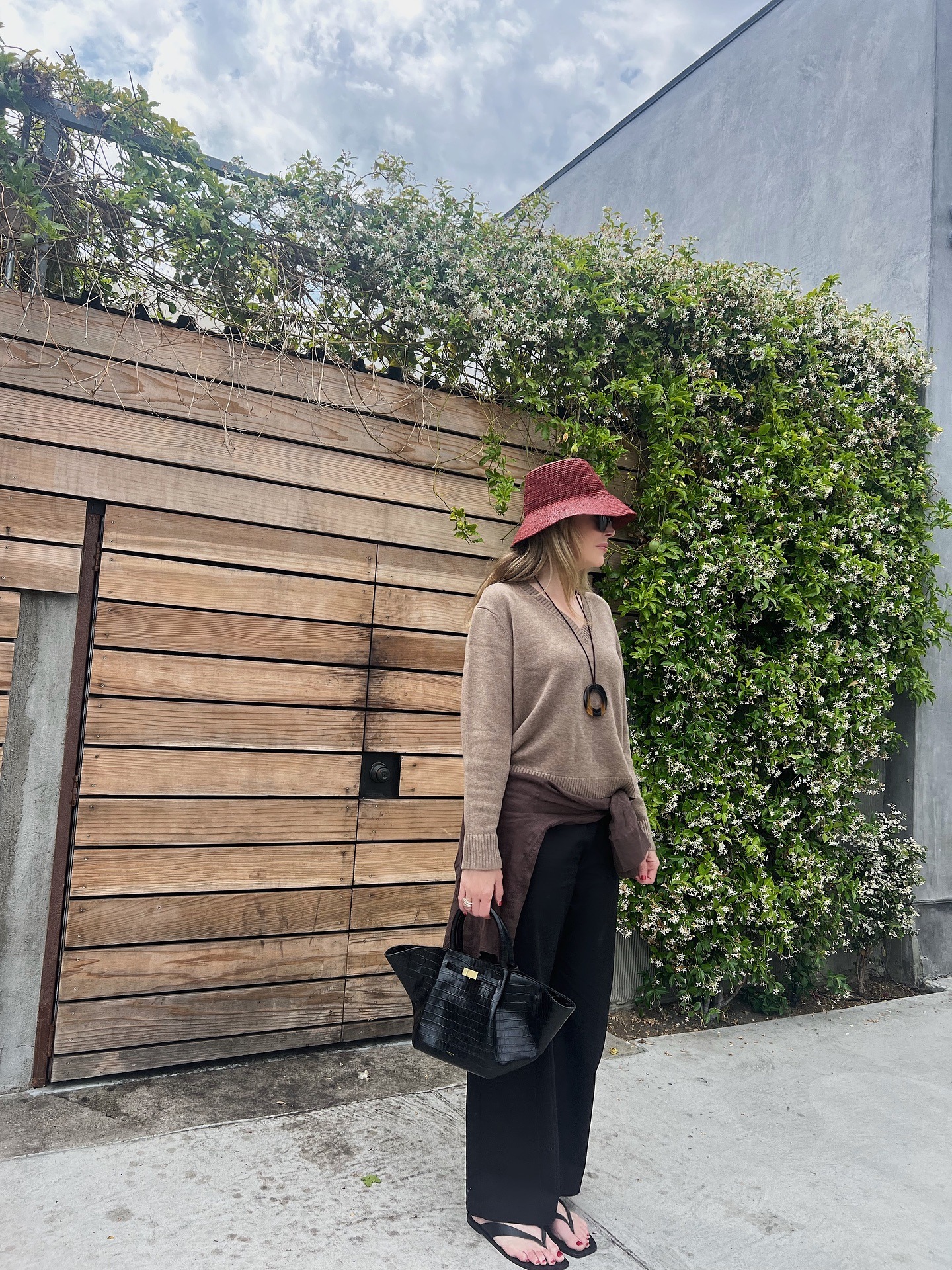 Jen Andrews Cater wearing a brown sweater, black trousers, flip-flops, and a statement necklace.