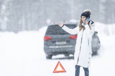 Driver who crashed the car off the slippery winter road calls towing service with emergency triangle next to her outside the car.