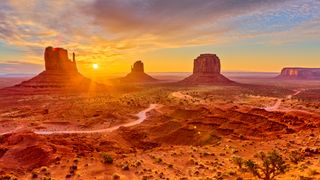 Monument Valley at sunset with large rock formations and a partly cloudy sky.