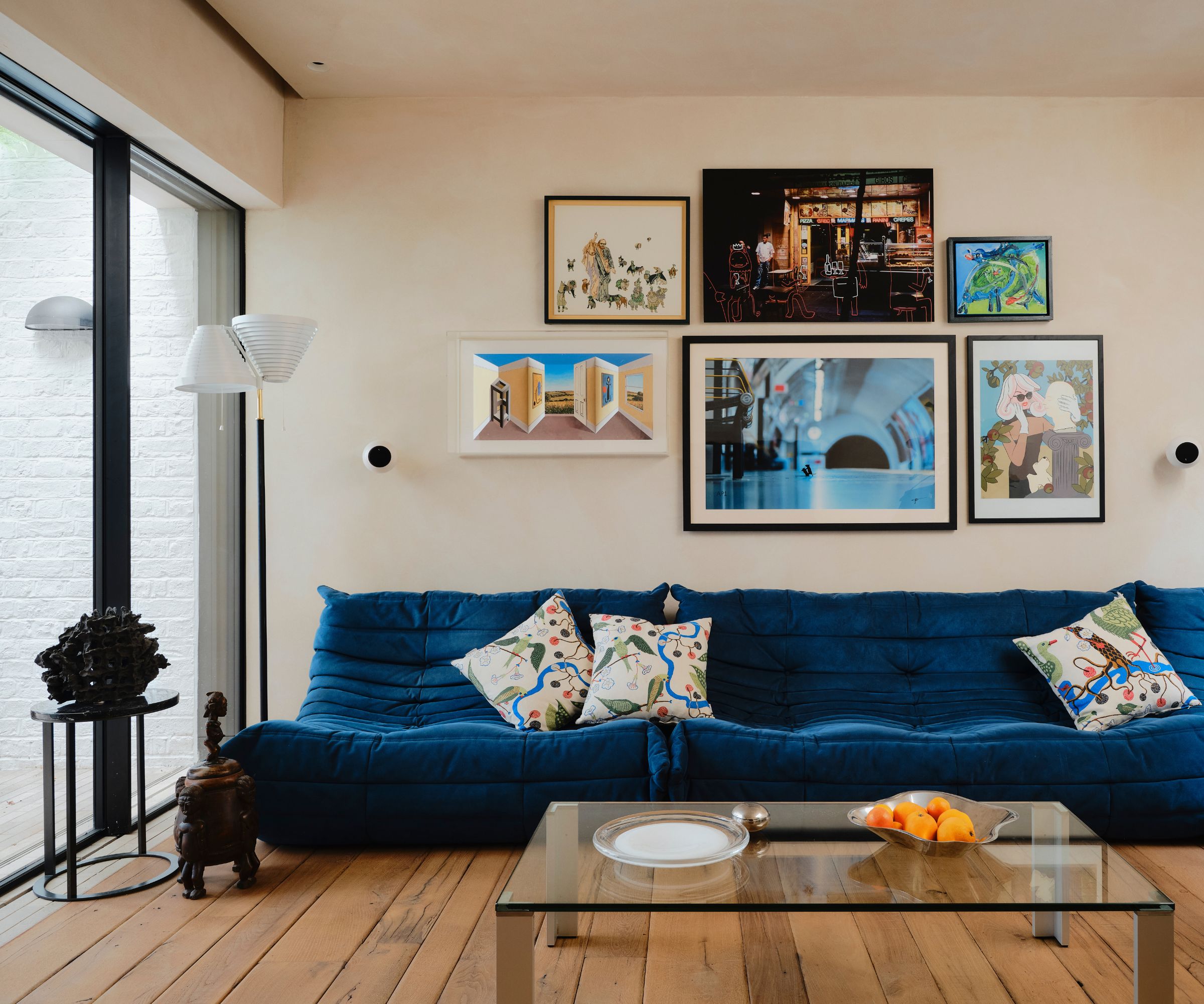 Cream living room with large blue sofa, a glass coffee table and a gallery wall