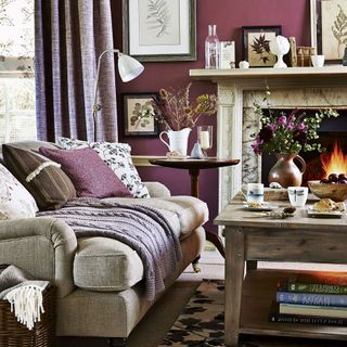 A traditional living room with dark purple walls and curtains and a roaring fire