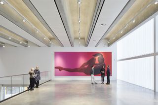 A walkway with a glass railing and a large painting of a ballet dancer at the end of it.