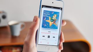 A person holding a blue apple iPod touch (7th generation) with a song playing on the screen