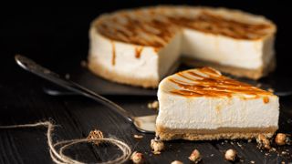 A slice of cheesecake cut from a whole cheesecake and drizzled in caramel sauce