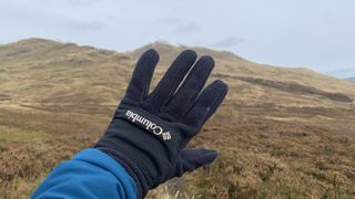 A hiker's hand wearing the Columbia Women's Fast Trek III Fleece Gloves with mountains in background