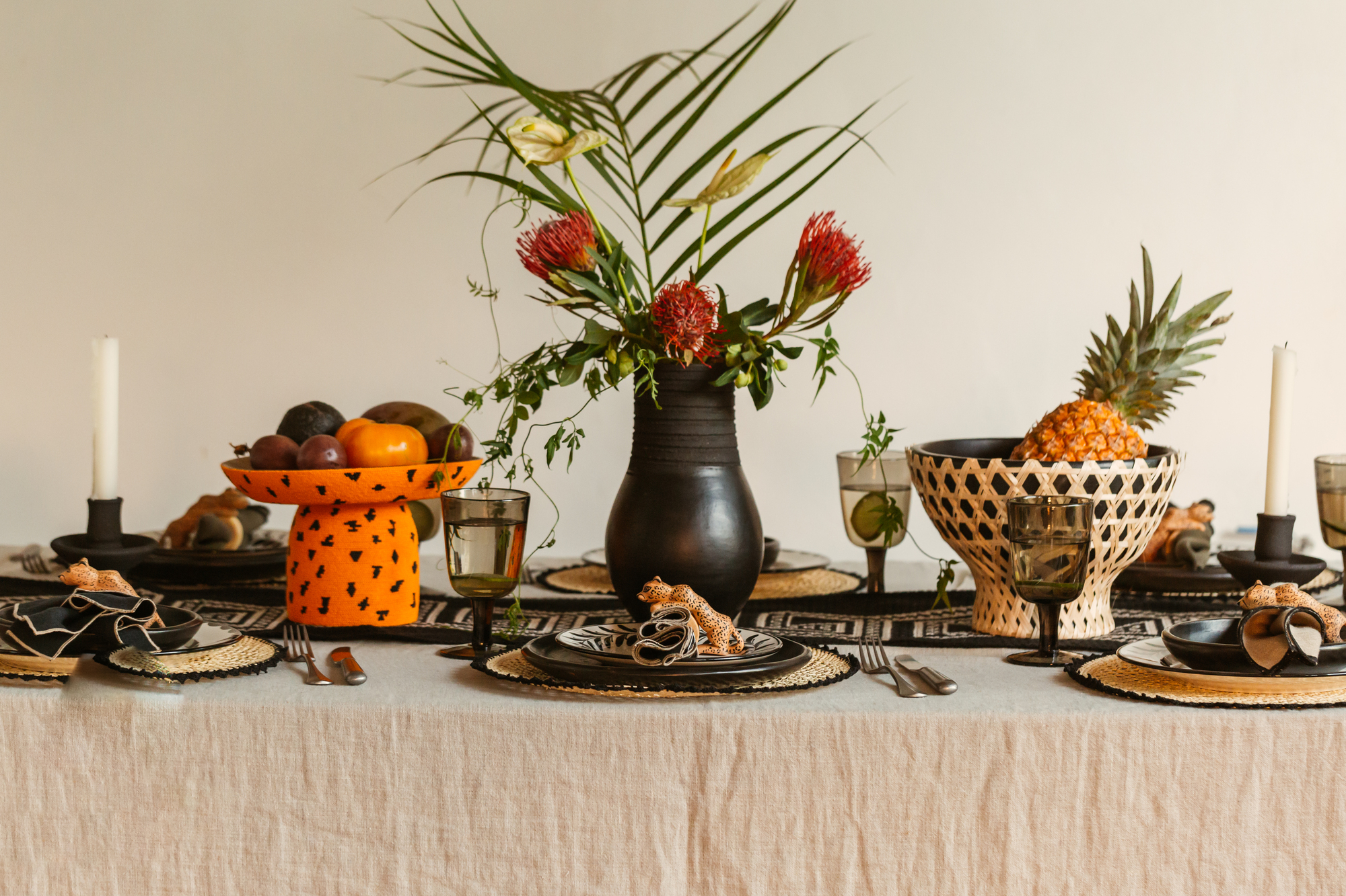 A themed tablescape with placemats, black plates, and a black vase centerpiece with a floral arrangement flanked by two fruit bowls