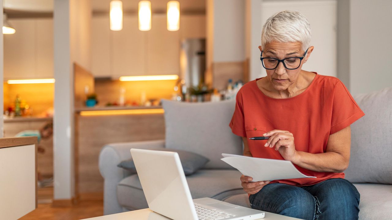 Senior reviewing paperwork at her laptop in her kitchen area