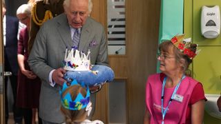 King Charles III holds a blanket with a paper crown on top during a visit to open the Priscilla Bacon Lodge hospice, a state-of-the-art palliative care unit which has been specially designed to allow patients to enjoy the surrounding landscape, working in partnership with Norfolk Community Health and Care NHS Trust on October 26, 2023 in Norwich, England.