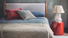 Neutral bedroom with blue walls, red round bedside table, white lamp, and colorful cushions.