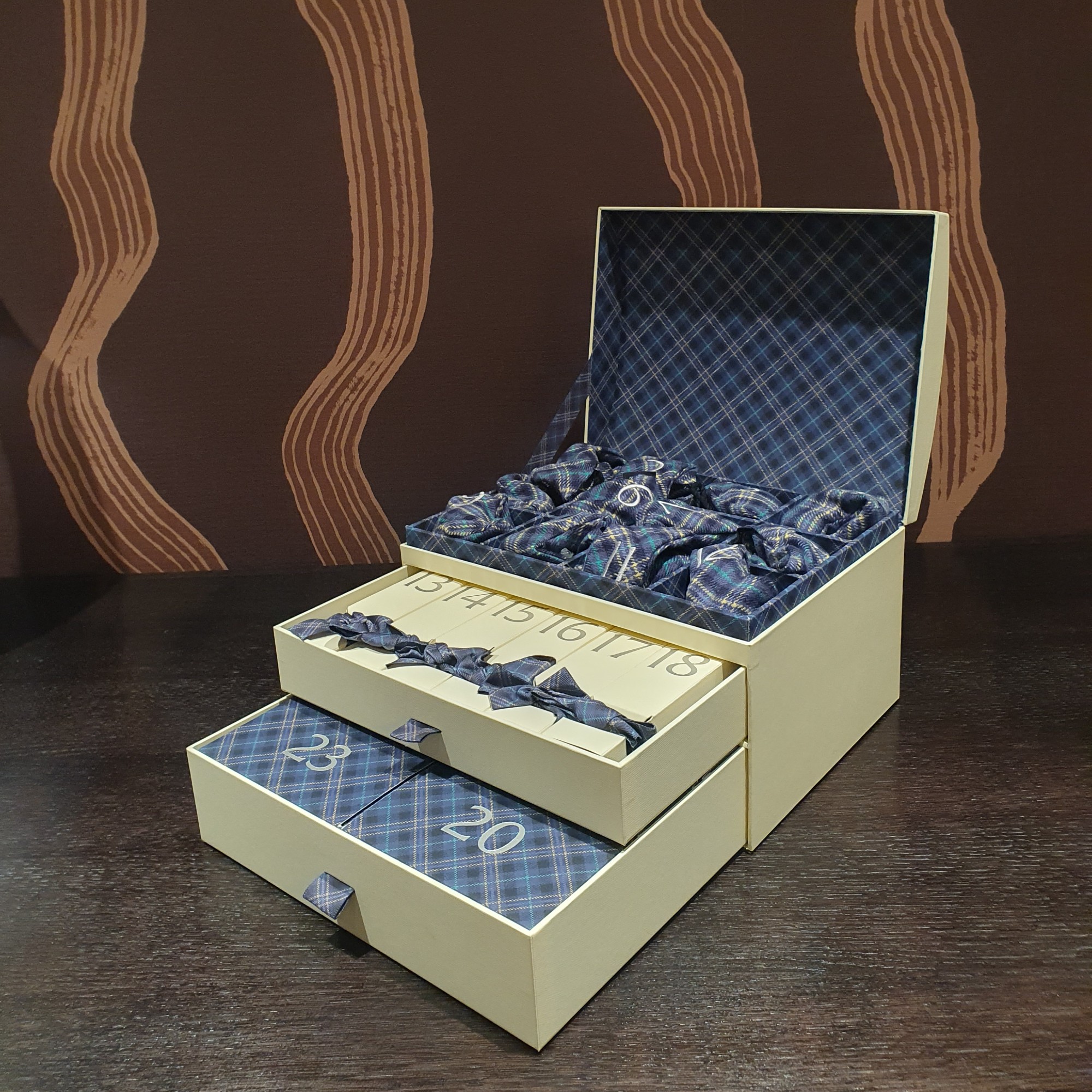 An open Jo Malone luxury advent calendar for 2026 set on a dark wood table with a brown patterned wallpaper in the background