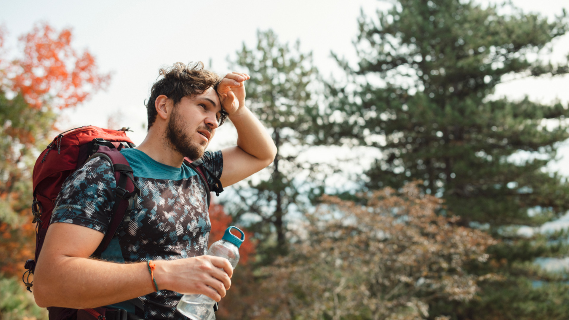 A man wiping sweat off his forehead on a hike