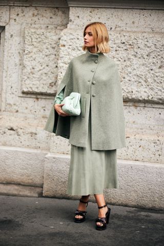 A woman at Milan Fashion Week's Fall 2025 Street Style in a green cape coat, green dress, and brown platform heels