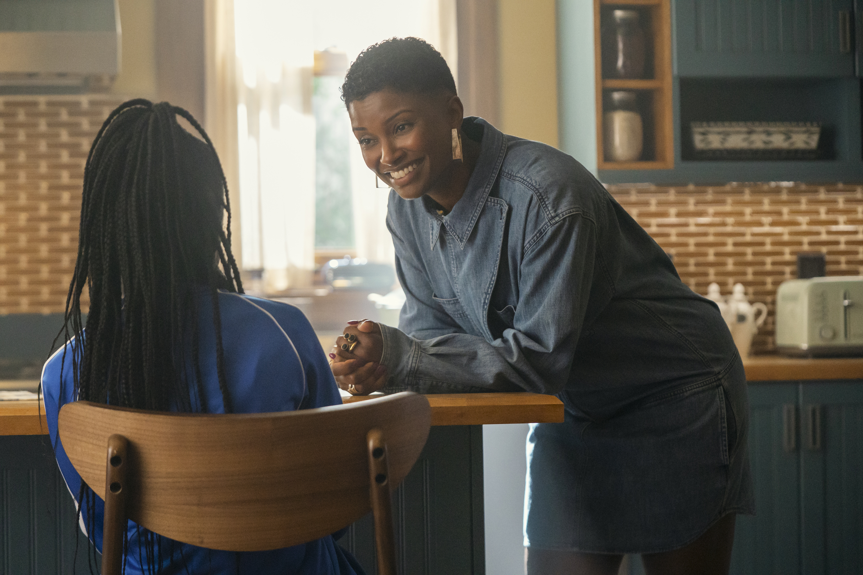 Elle Monteiro (Samantha Walkes) leans over a table smiling while talking to a child in cross season 2