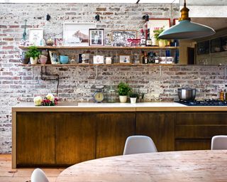 A rustic exposed brick wall with open shelving and distressed brass cabinetry.