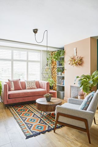 Peach living room with mid-century sofa and armchair, wall shelving, pendant light and wood coffee table with boho theme