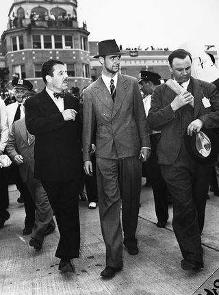 HOWARD HUGHES (1905-1976). /nAmerican industrialist, aviator, and film producer. Hughes (center) photographed with Grover Whalen, President of the New York World's Fair (left), and Al Lodwick, Hughes' flight manager and press agent, after arriving at Floy