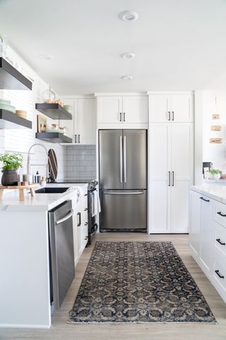 a small kitchen in a galley layout with white cabinetry, wood flooring, large American style refrigerator and antique style rug