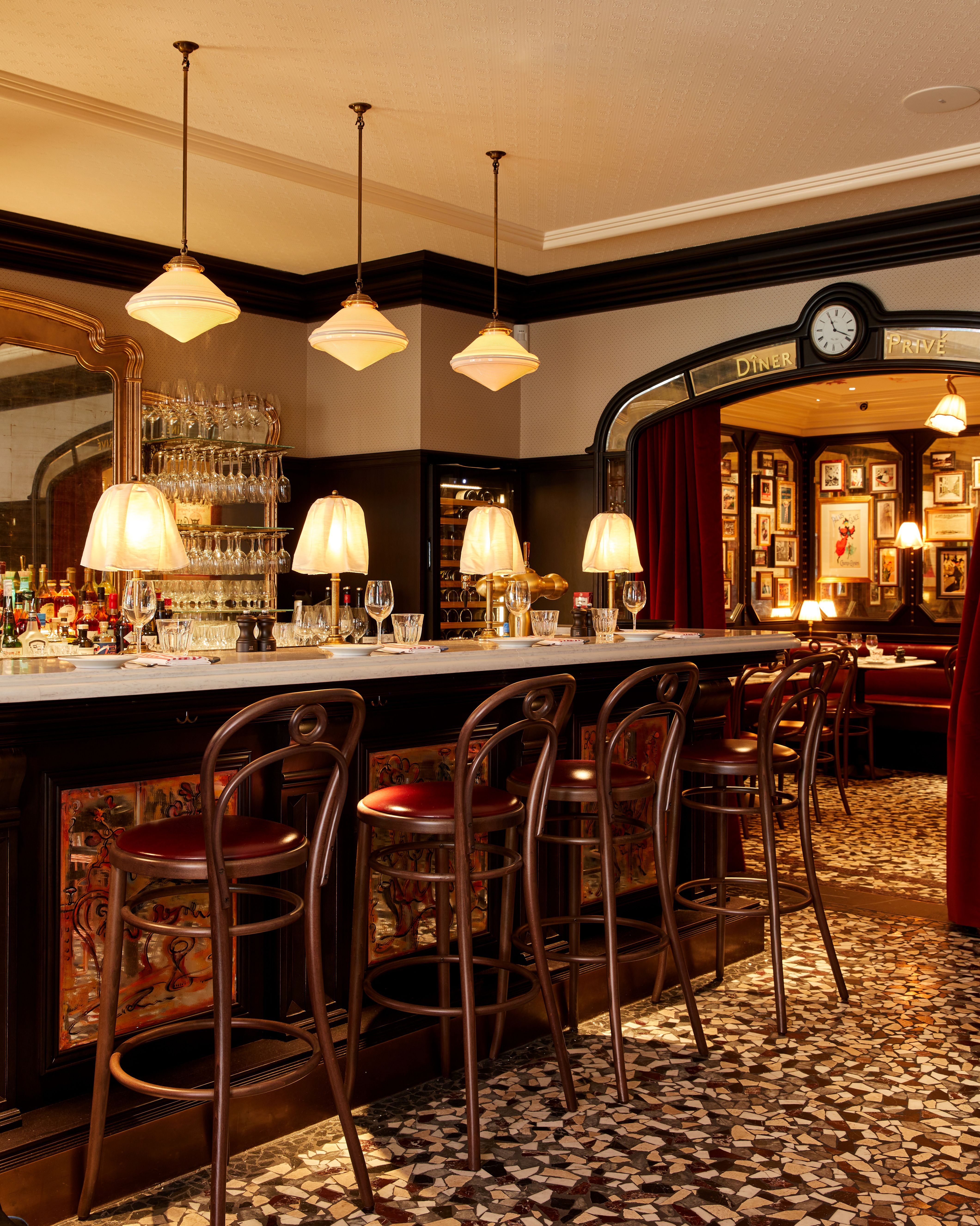 A series of images capturing the timeless interiors of a French-style bistro, filled with uniquely framed artworks, handpainted murals, golden-lit table lamps, wooden furniture, red velvet banquettes, food, and more.