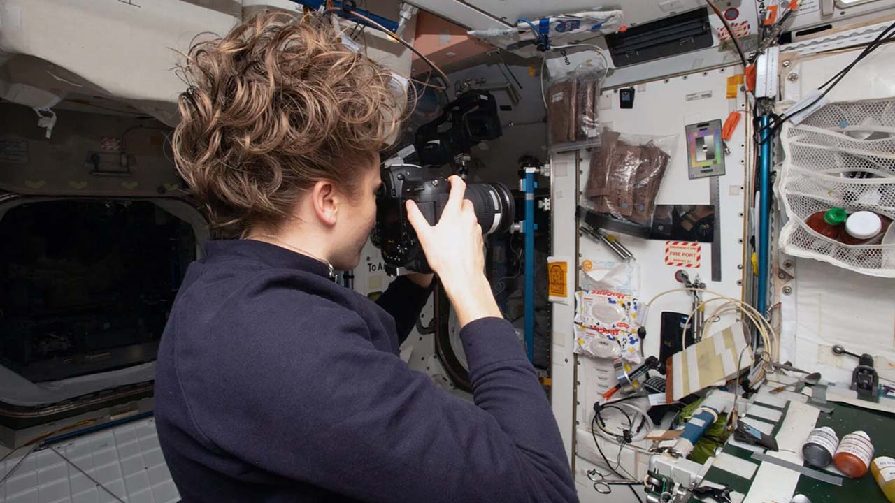 an astronaut with a camera aiming at a series of objects mounted on a wall