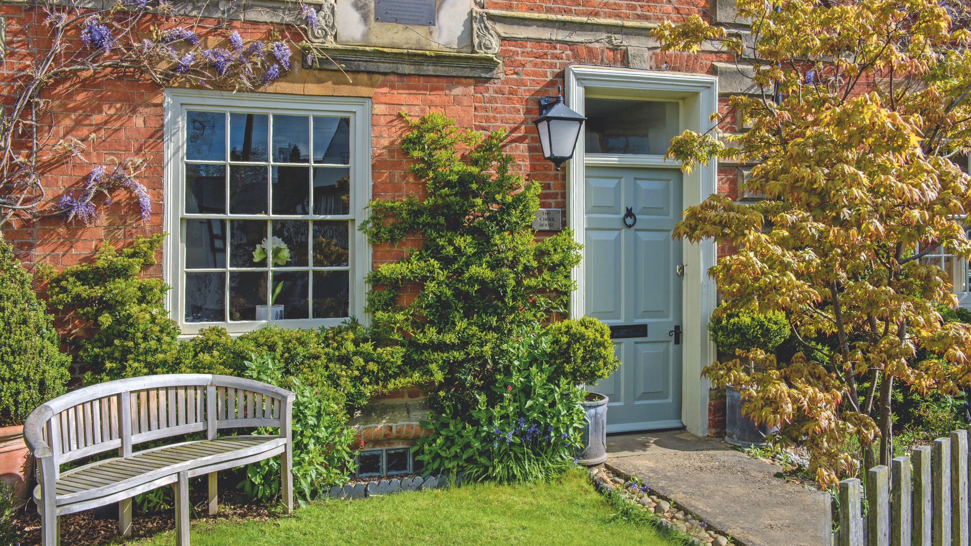 Victorian house with a blue door, a wooden bench in front of it, and plants growing up the brick