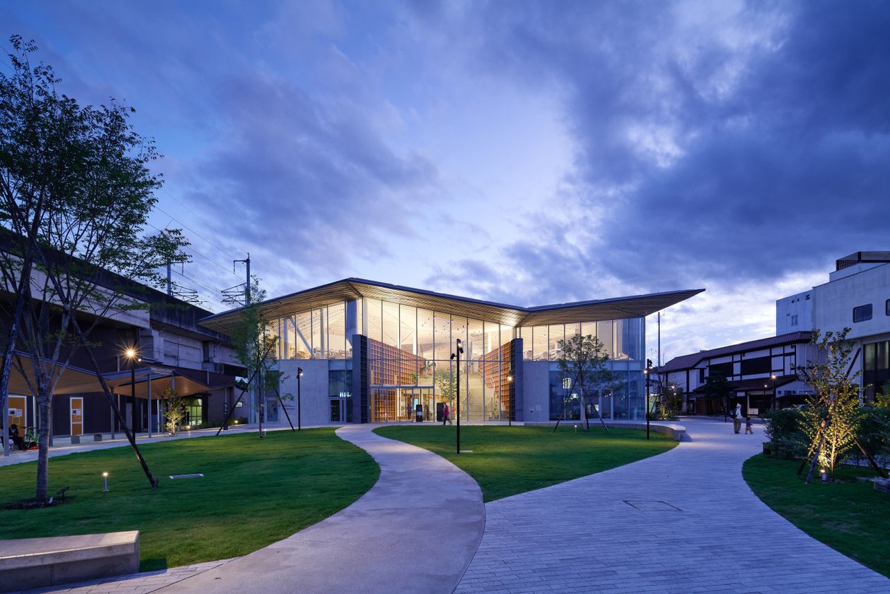 The Nasushiobara library at night which features a kite-style roof and ground to roof panel windows. 