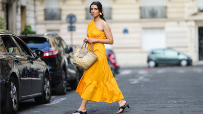 Ketevan Giorgadze @katie.one wears a one shoulder cut out maxi dress in orange from Mango, oversized golden hoop earrings from Zara, flip flop heeled black sandals shoes from APC Paris, a Le Grand Panier beach straw bag by Jacquemus, on August 12, 2021 in Paris, France. (Photo by Edward Berthelot/Getty Images)