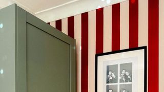 Bedroom with red and cream stripes on wall next to green furniture and pic of people on wall