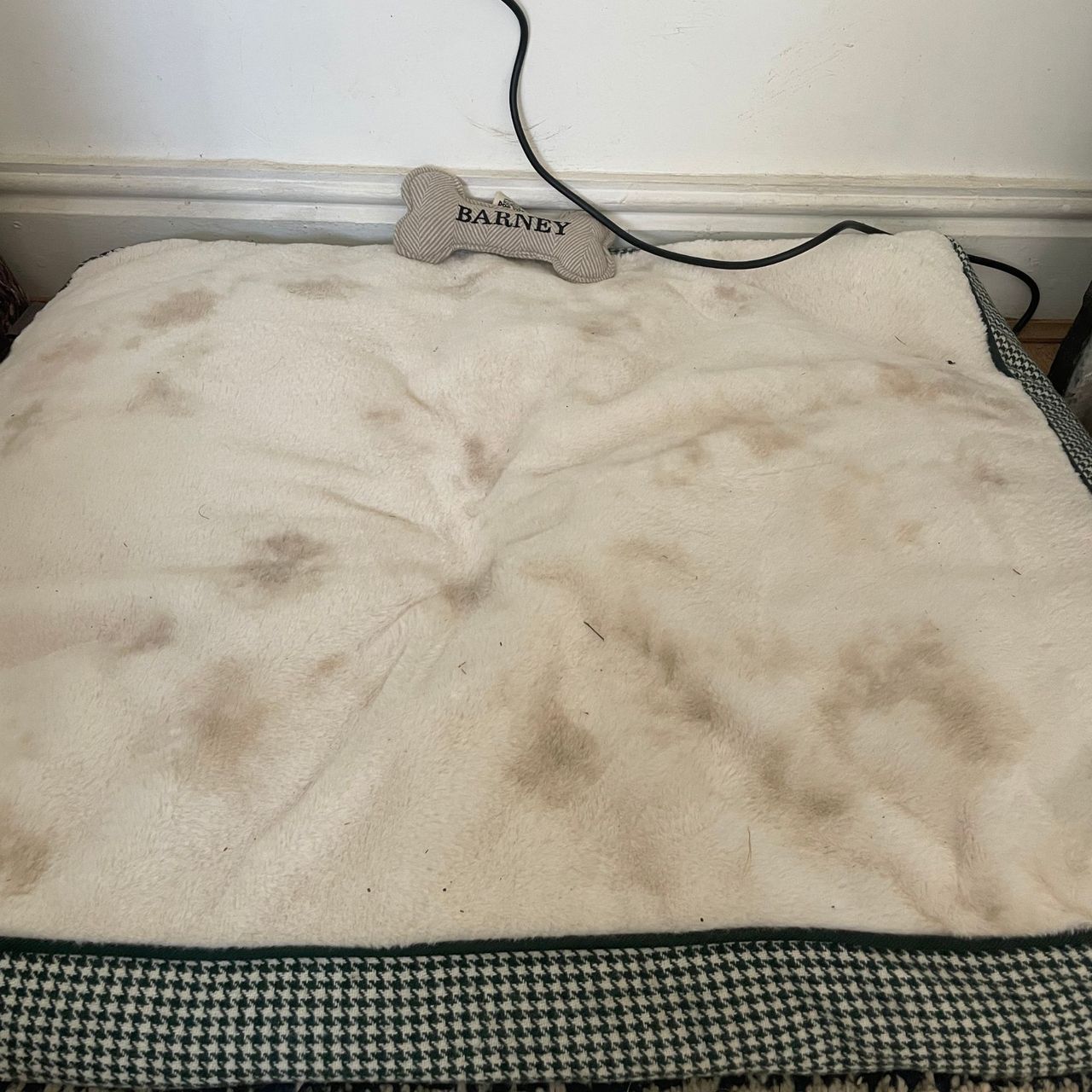 White dog bed with herringbone edging, with muddy paw prints all over it